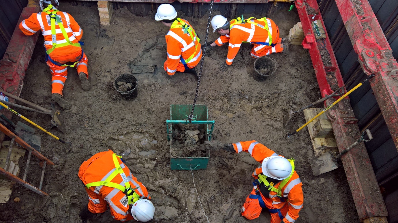 A picture of five workers  in PPE doing an archaeological excavation  