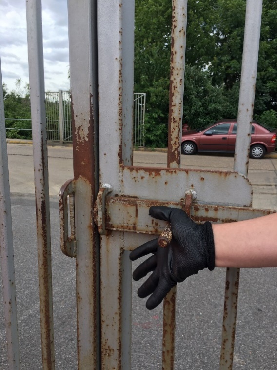 Picture of an unsafe gate closing with a gloved hand trying to close it with a risk of hand entrapment and pinch that can cause hand entrapment and pinch point