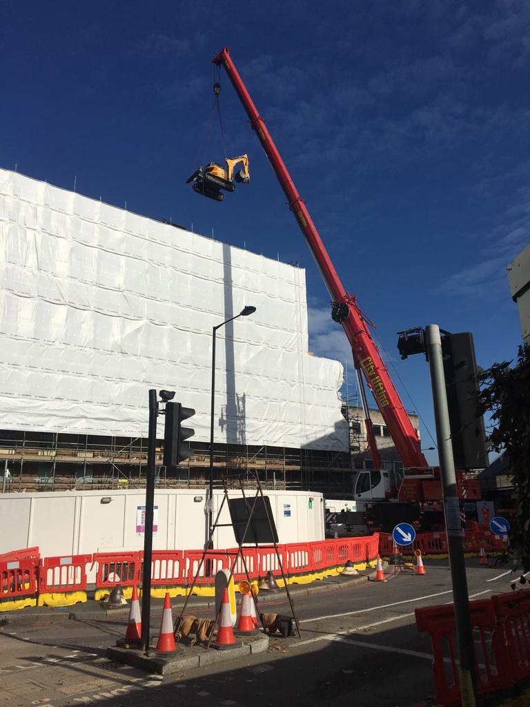 An attendant crane in front of a building lowering a machine 