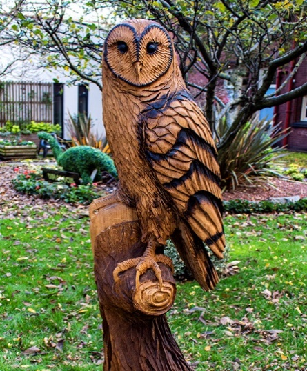 A picture of wood carved owl in a green space 