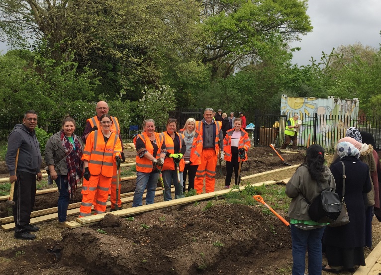 A group of people standing in Ward End Park by raised planter beds 