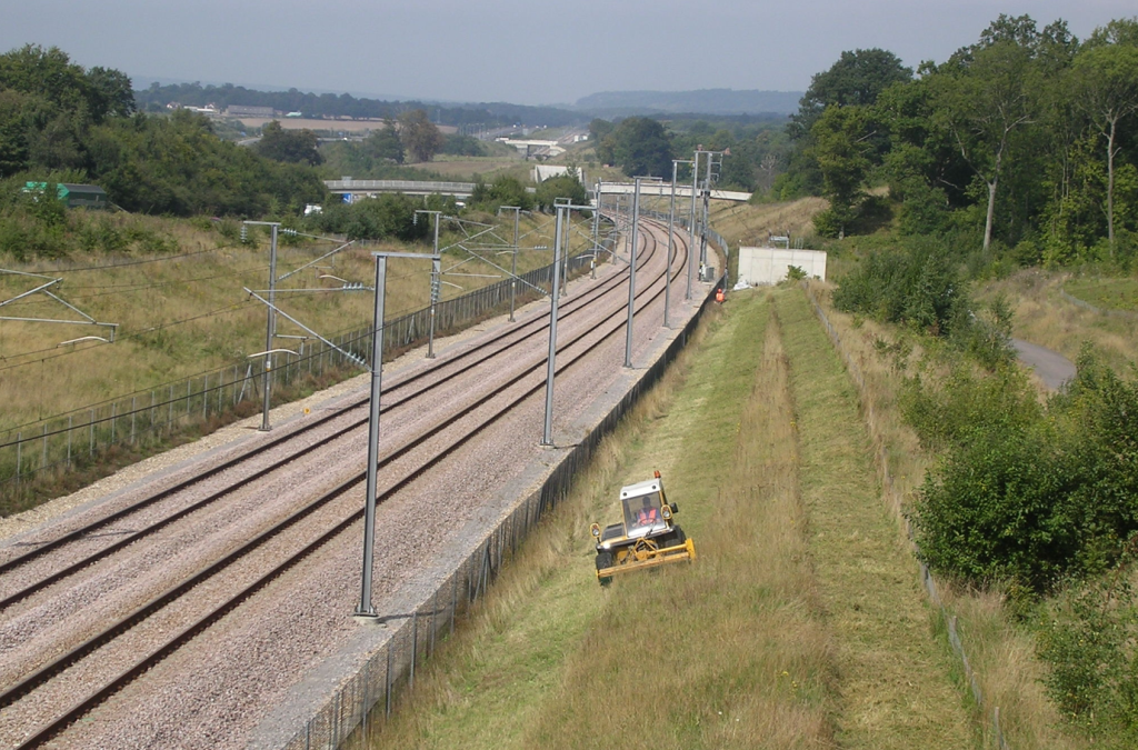 Picture of grasscutter vehicle cutting grass alongside rail tracks that are fenced off