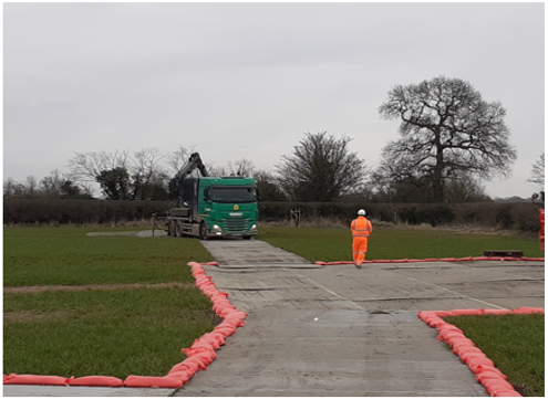 A picture of a road with a truck and worker and sealed trackway with sandbags